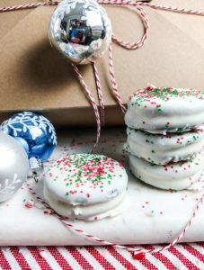 Chocolate dipped Oreo Christmas cookie stacked by gift box. OnTheGoBites.Com